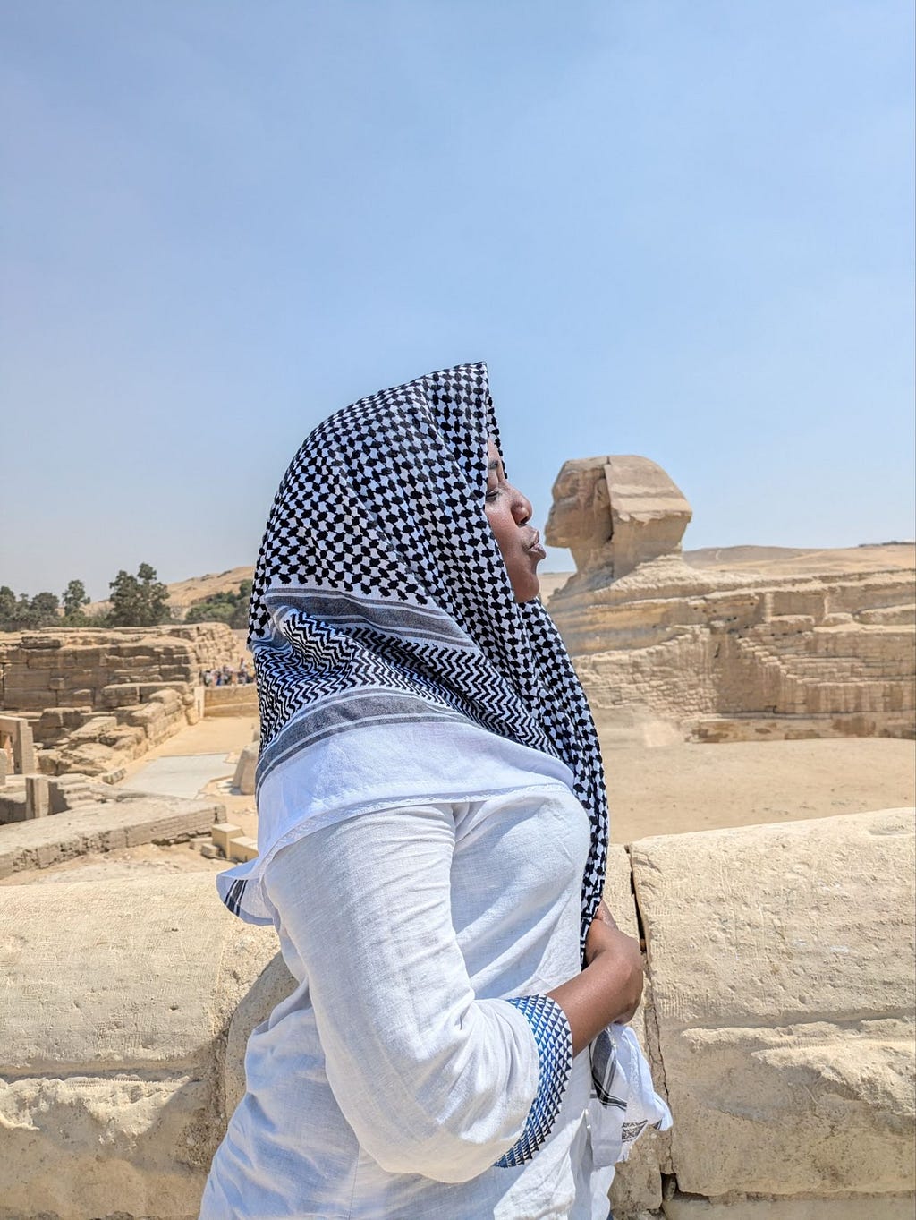 The author, Amani Ali, is in the foreground and the Sphinx is in the background. Amani is posed as if she is kissing the Sphinx.