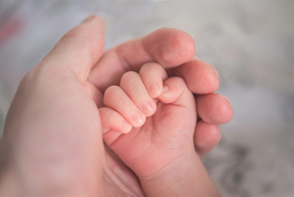 Close-up photo of a grown-up hand holding the hand of a newborn