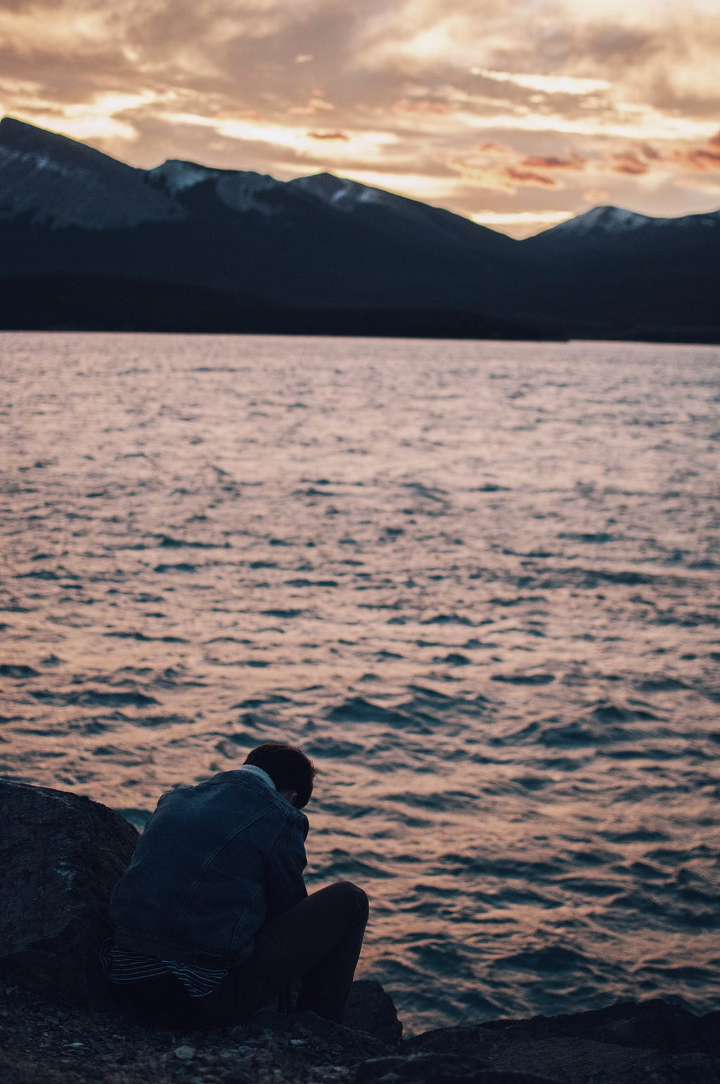 A boy sitting alone by the shore at dusk