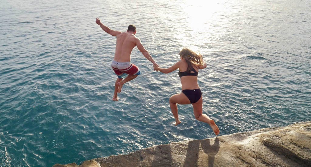 Couple jumping off cliff into ocean on date