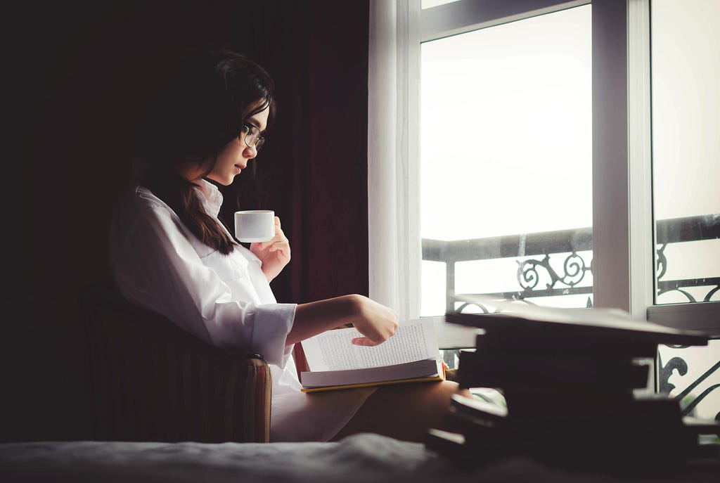 a woman is reading a book, drinking coffee
