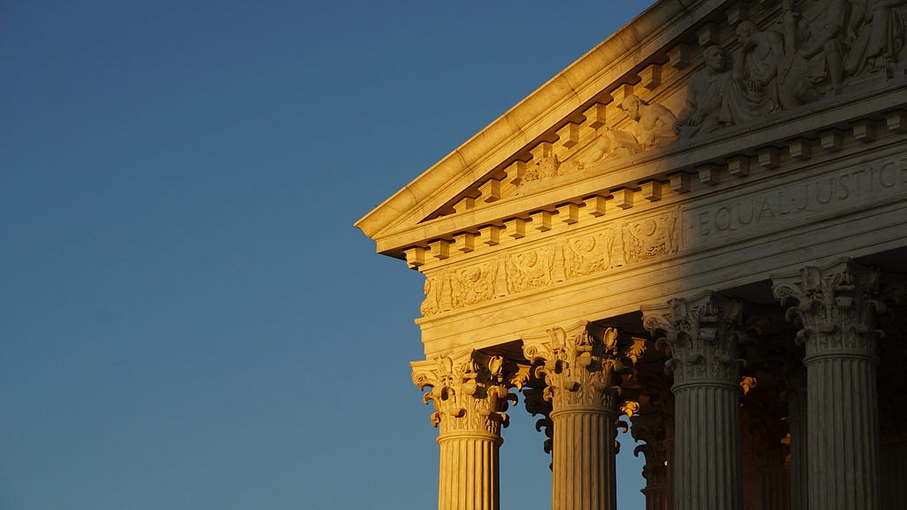 The sun shines on the facade of the U.S. Supreme Court with a blue sky behind it