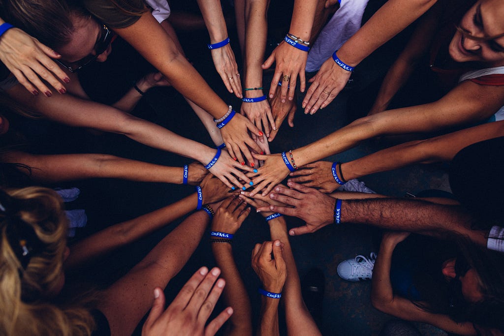 A group of many people’s arms reaching to touch hands in the centre of a circle, symbolizing togetherness and unity.