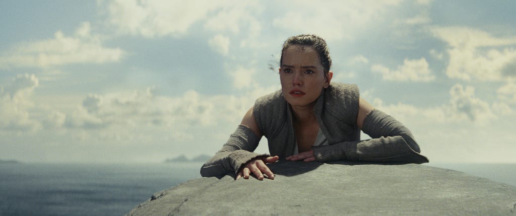 Rey lays flat on a rock on Ach-To, staring out into the distance facing the camera, distressed about her next move.