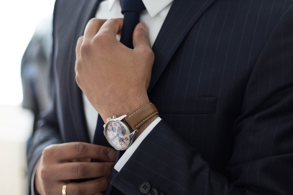 A man in a suit tightens his tie. He’s wearing an expensive watch on his wrist.