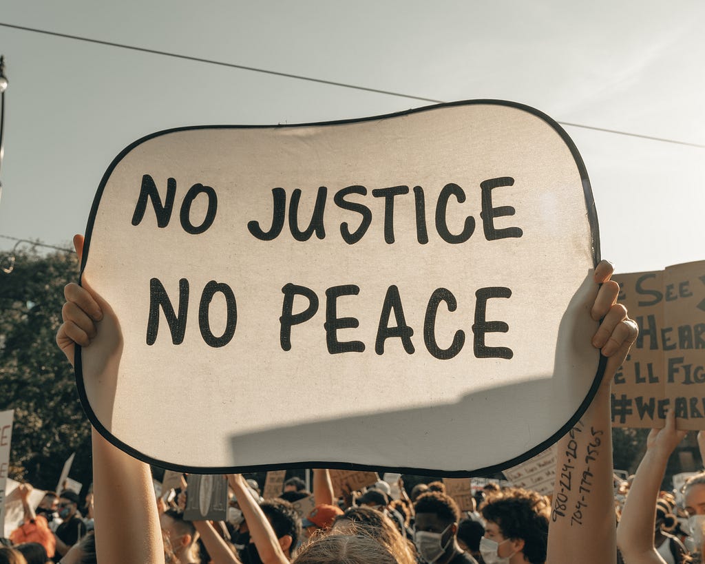 A person holding a board printing with “NO JUSTICE NO PEACE,” who was a member of a protest.