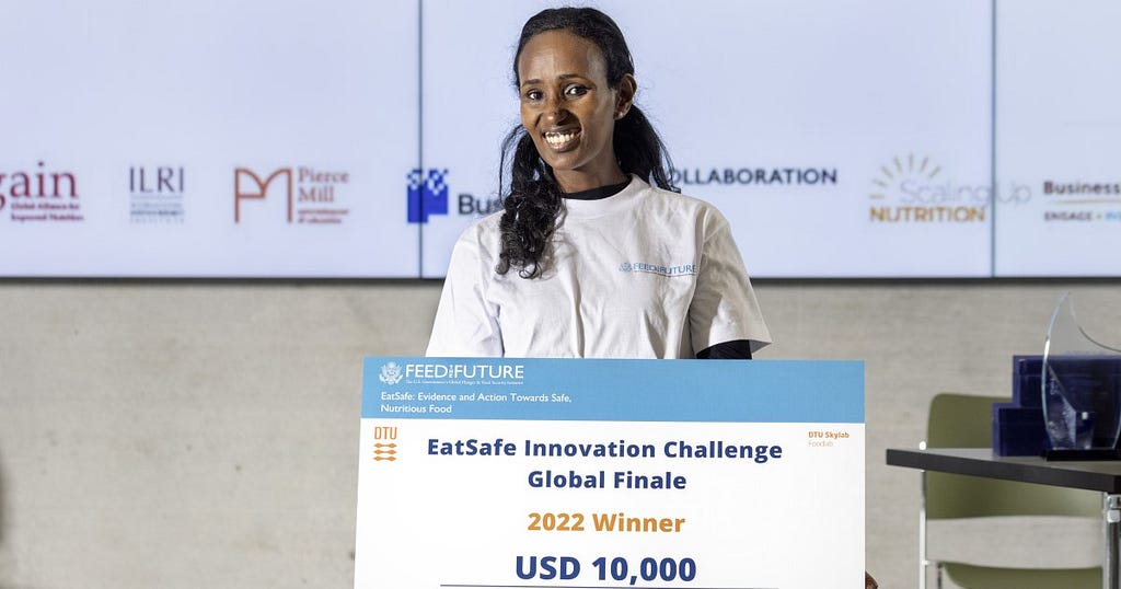 Helen Weldemichael holds a large check that reads: “EatSafe Innovation Challenge Global Finale 2022 Winner USD 10,000.”