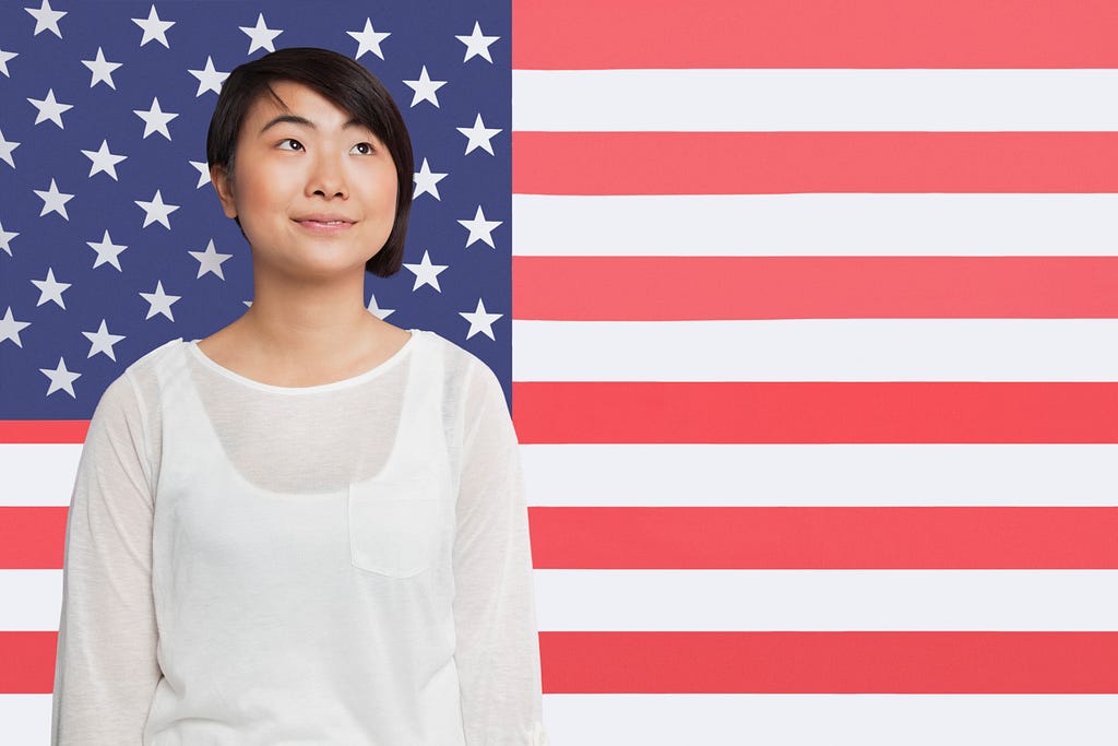 An Asian woman looking away behind an American flag as a background