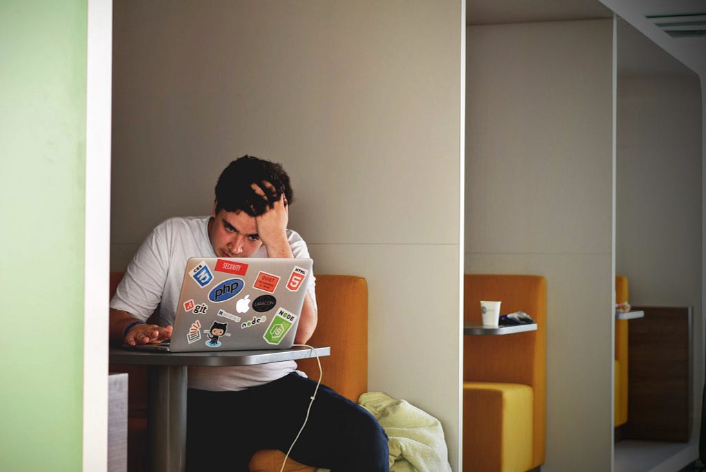 A man sat in front of a laptop computer with his head in his hands, looking stressed