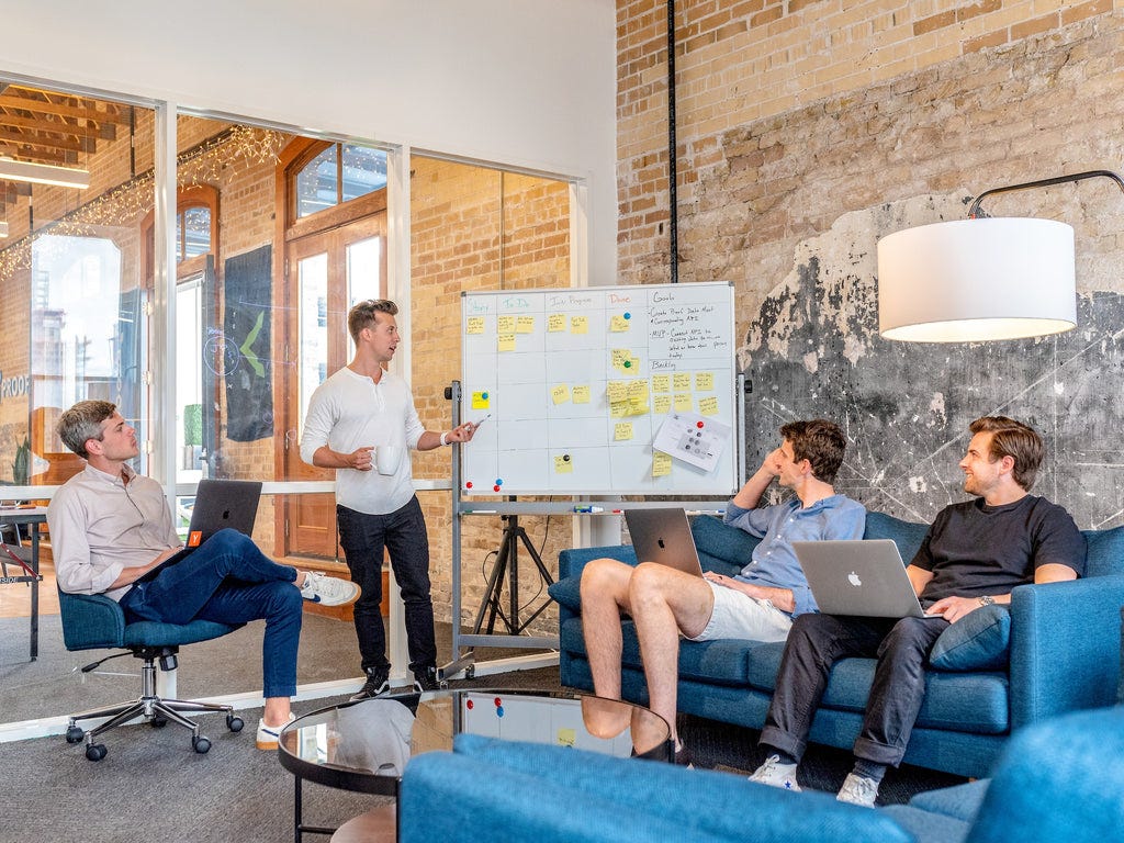 four gentlemen in a room with one presenting something on a whiteboard.