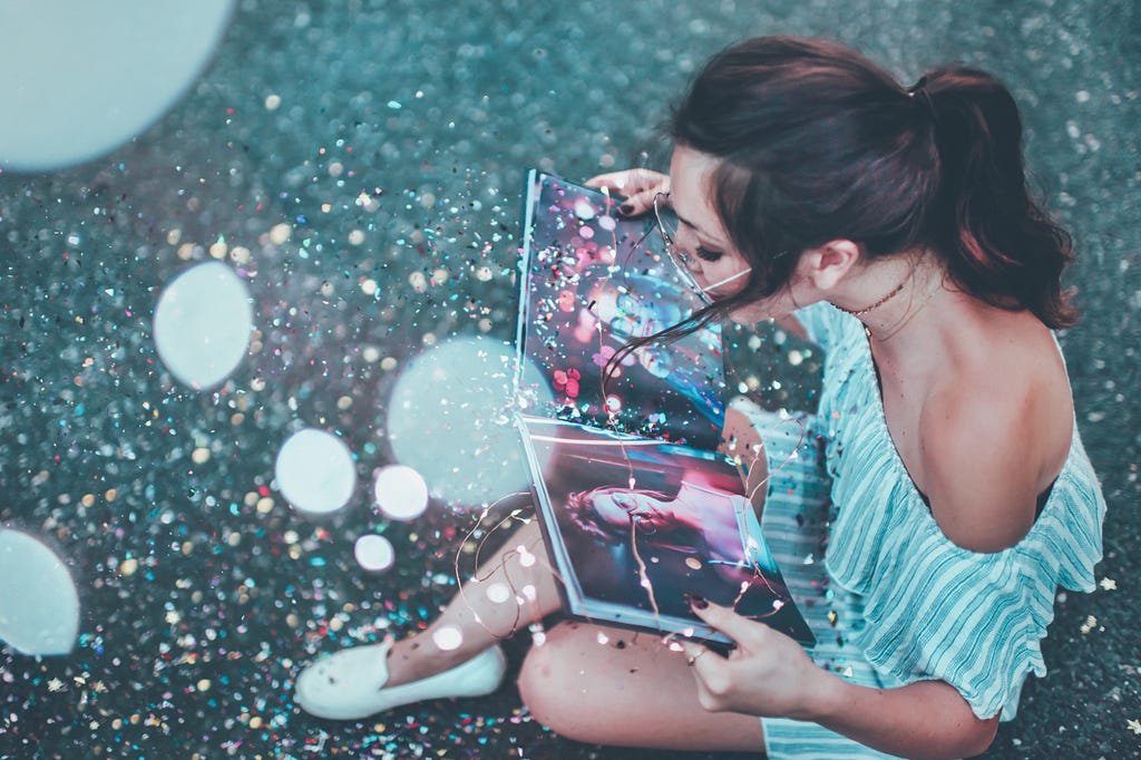 A girl sitting with her vision board- journal in her hand, sparkles all around her, surrounded by magic!