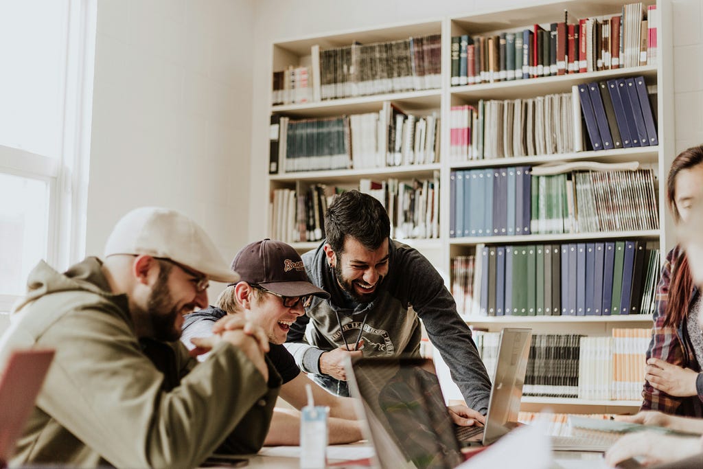 A group of people looking at a laptop in a library or learning room.