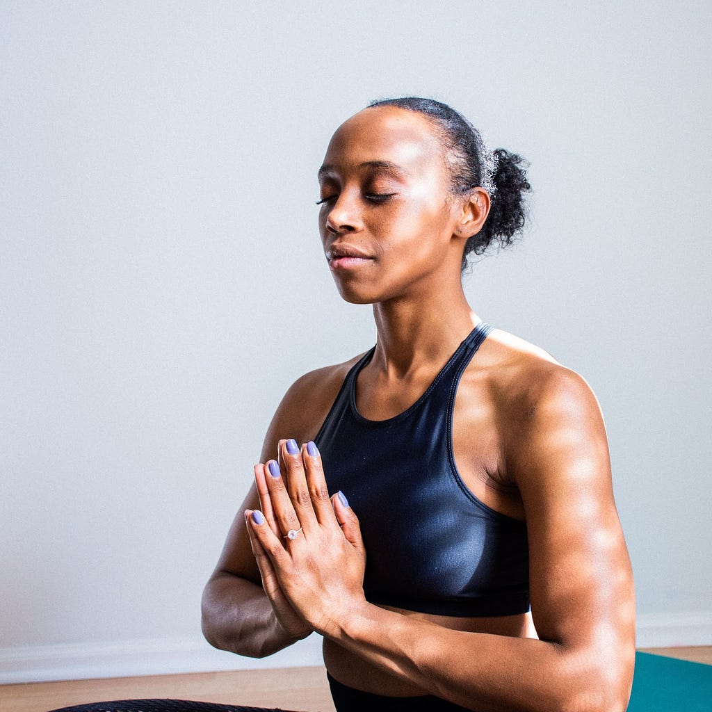 A woman sitting with eyes closed and hands in “namaste” gesture.