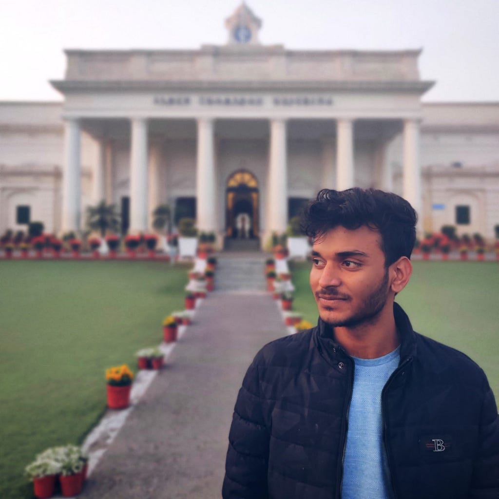 A person smiles, looking off to the left, and stands outside in front of a grand pale building with columns.