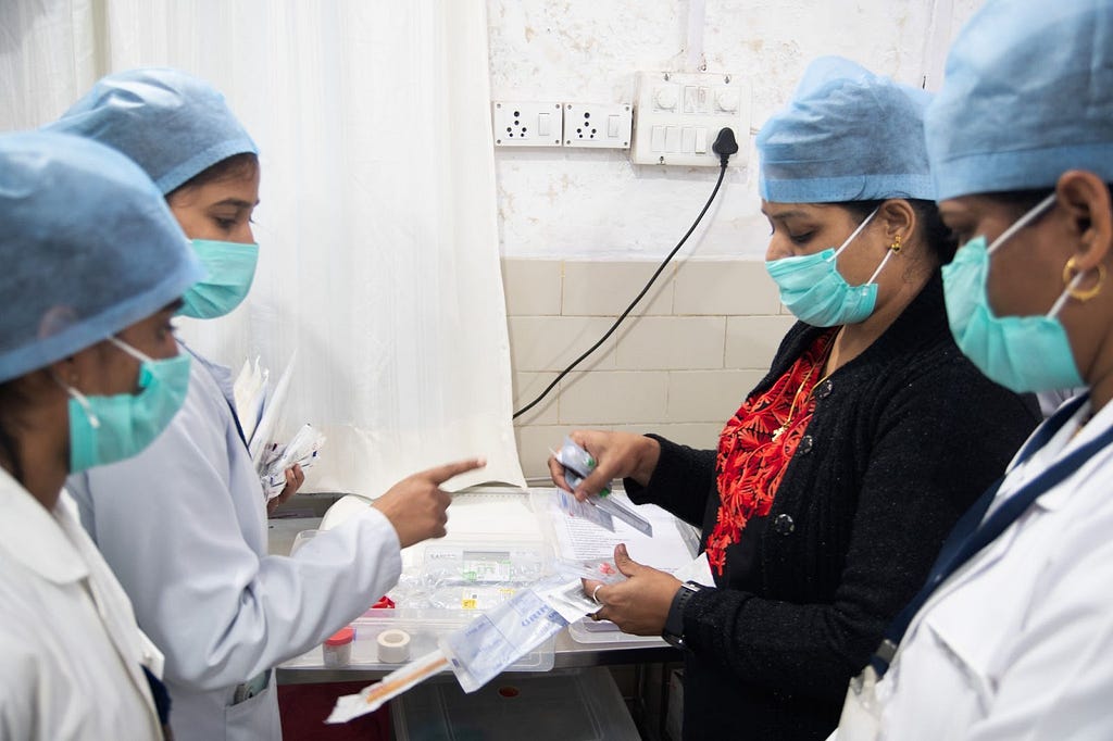 Four hospital nurses wearing masks and scrubs review drugs for a patient.