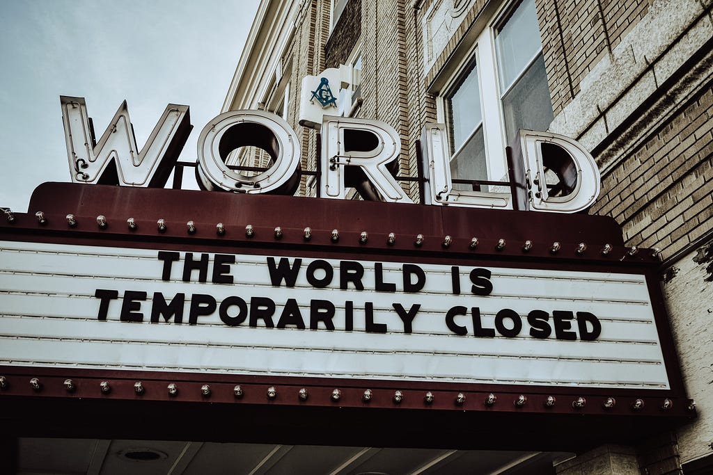 Placa de cinema de um cinema chamado WORLD, e em vez de mostrar filmes em exibição está a frase "THE WORLD IS TEMPORARILY CLOSED", que traduz livremente para O MUNDO ESTÁ TEMPORARIAMENTE FECHADO.