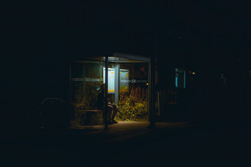 Shadowy figure sitting in a bus stop in the dark with a shallow light