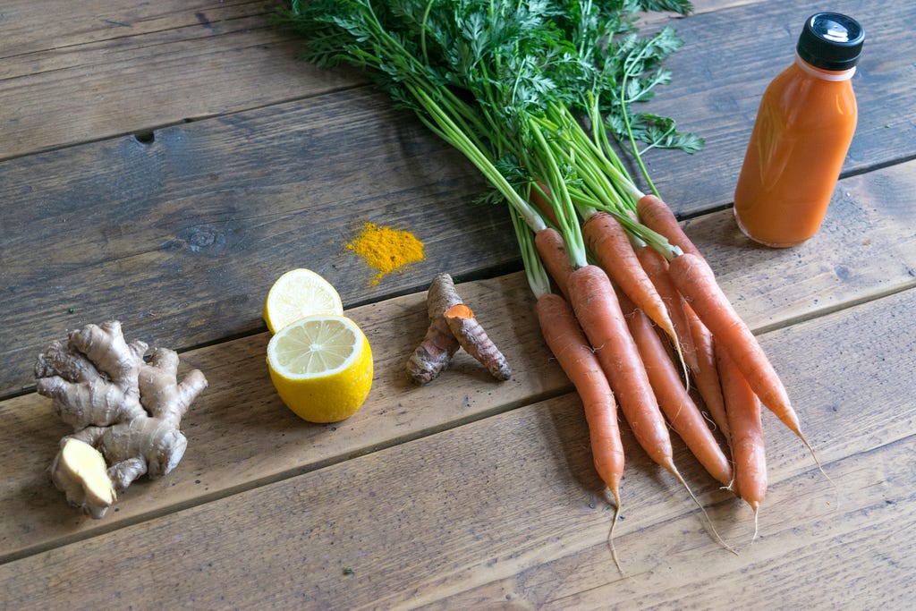 Ginger, lemon, carrots, ginger, and glass bottle of orange colored juice