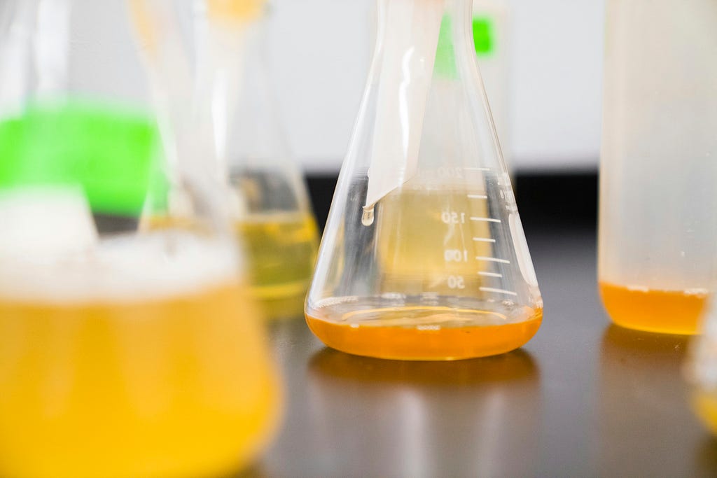 Vials full of orange liquid sit on a table in a lab.