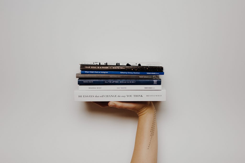 A person holding up a stack of books in their hand.