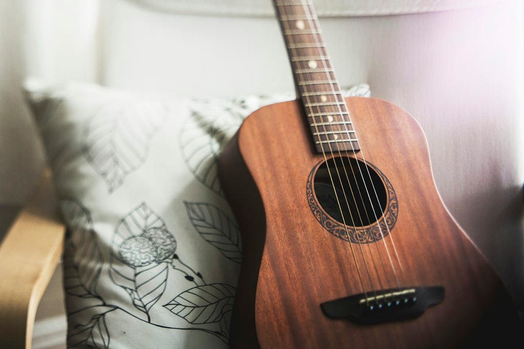 A guitar in front of an embrodered pillow.