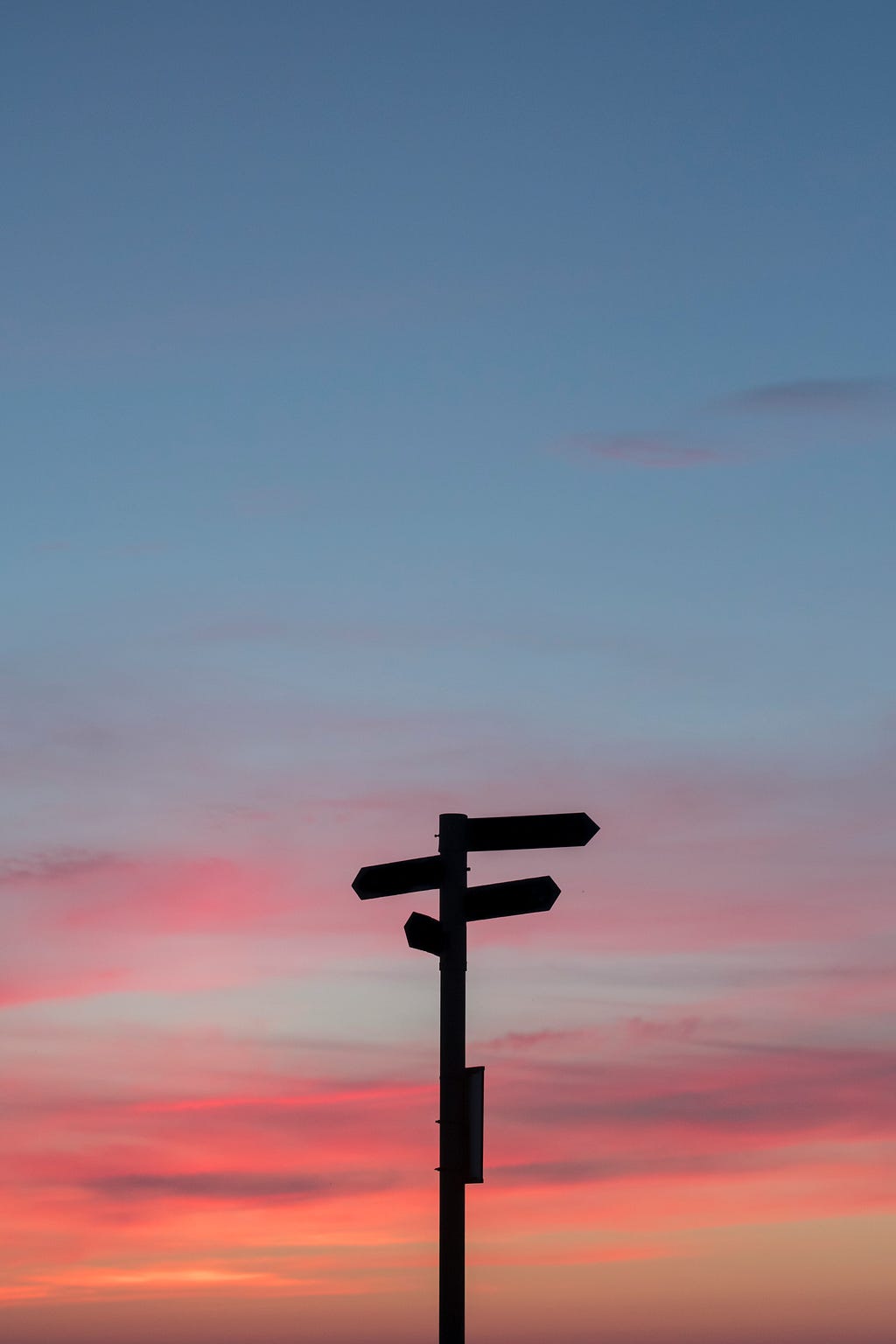 A signpost stands silhouetted against the sky at sunset.