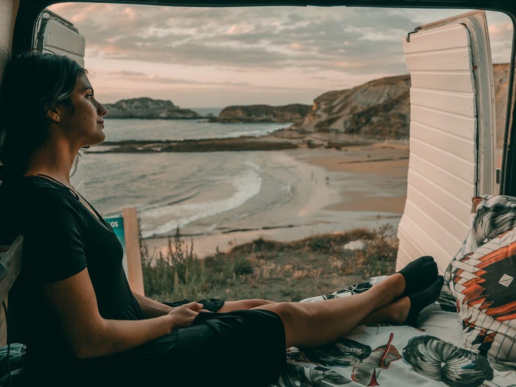 An individual sitting in a van with the ocean in the background.