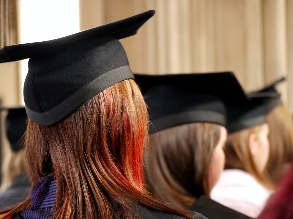 An image showing three students at their graduation ceremony, wearing mortar boards and facing away from the camera.
