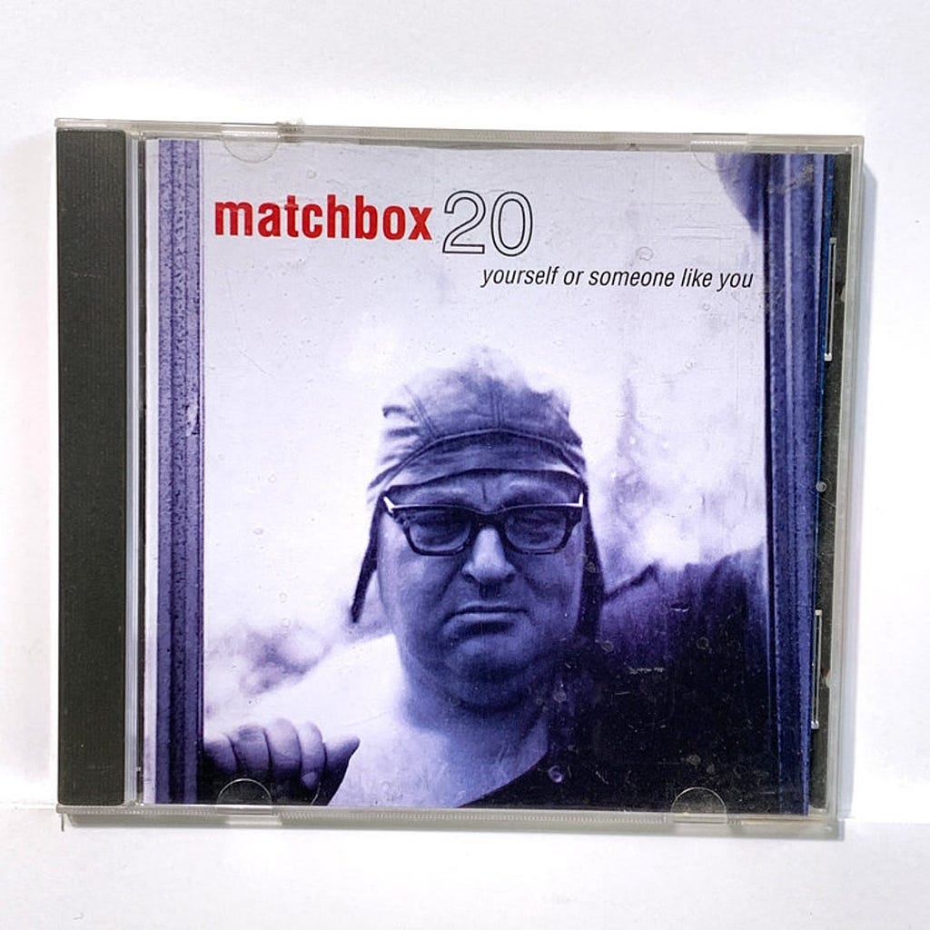 Album Cover for MatchBox 20 featuring a man in a fitting leather cap with glasses with his eyes closed. The cover is an indigo color.