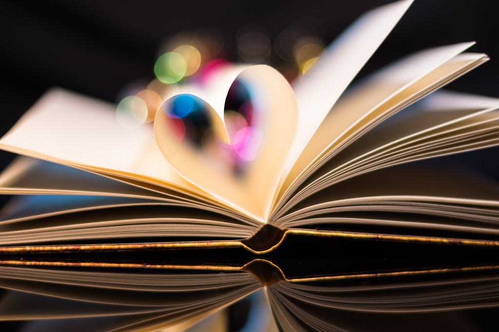 a paper book is open on desk with two pages folded together into spine to create a heart shape