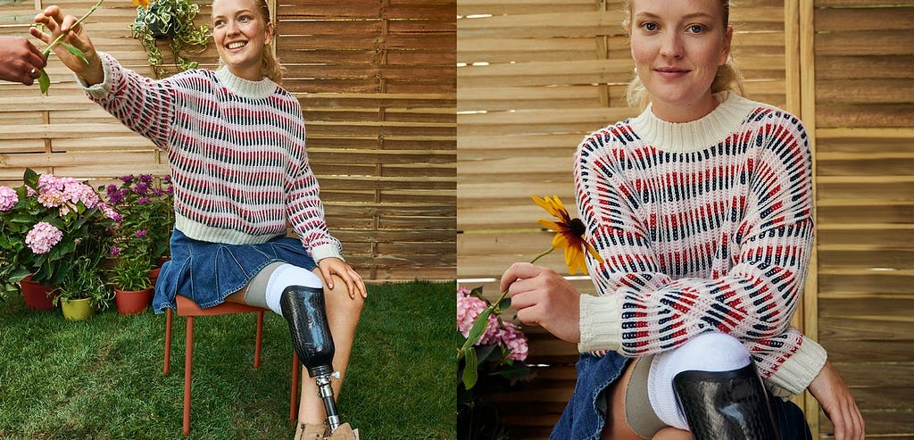 Image of a woman with a prosthetic leg, sitting in a chair, wearing a knitted jumper with standing collar and a denim skirt. She’s reaching out to grab a flower someone else is giving her, and she smiles.