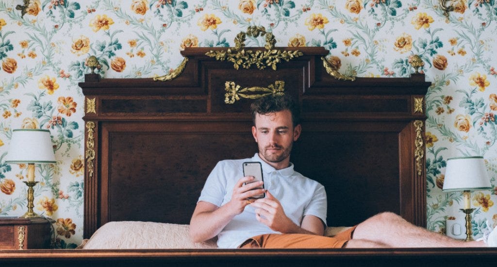 A man looking at his phone while sitting on a bed