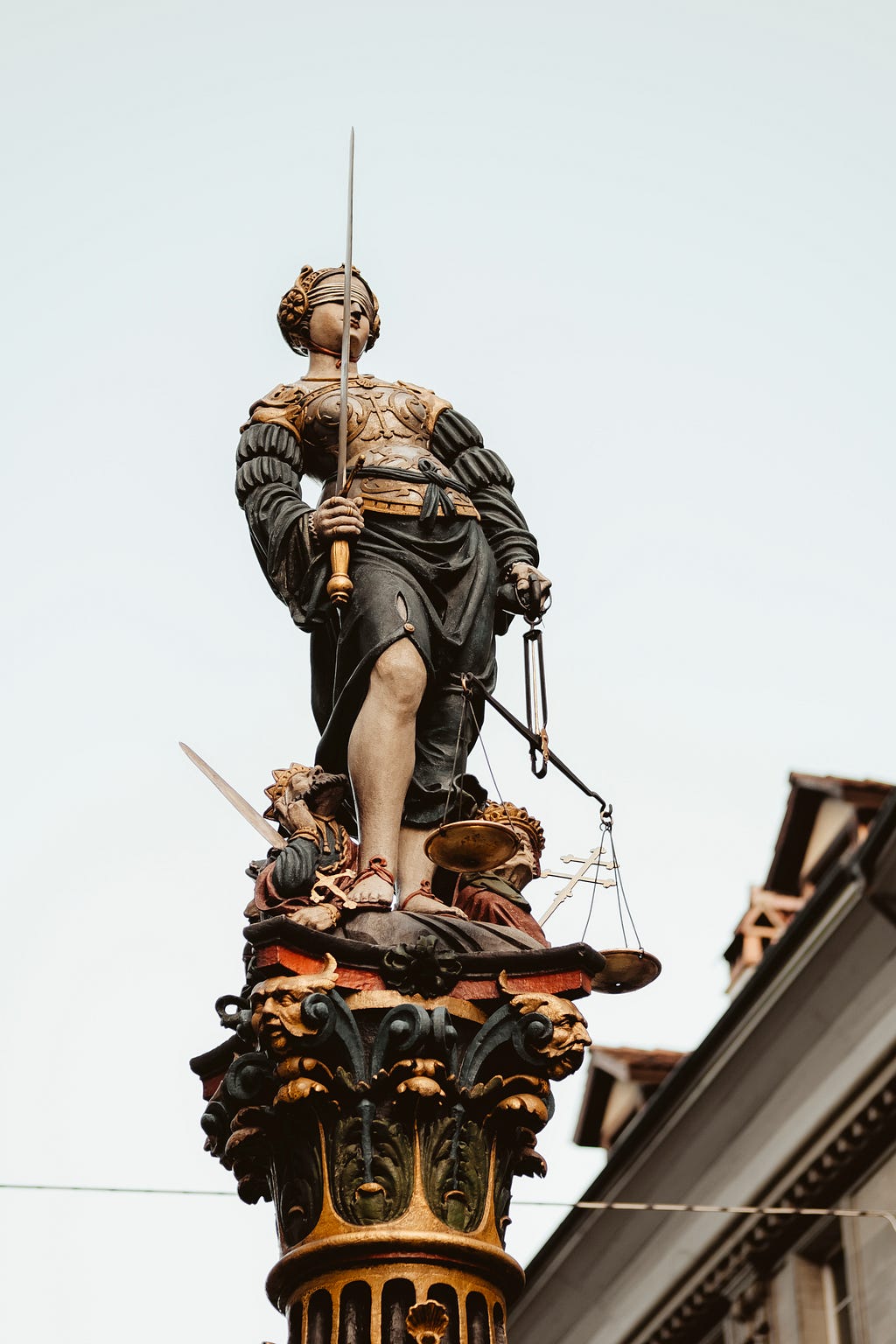 Lady Justice with her blindfold, sword, and scales looking standing tall above everyone on a pedestal