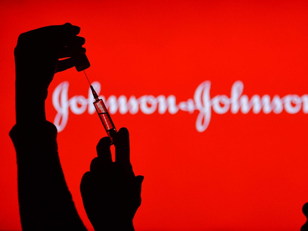 An individual administers a vaccine in front of a “Johnson & Johnson” sign.