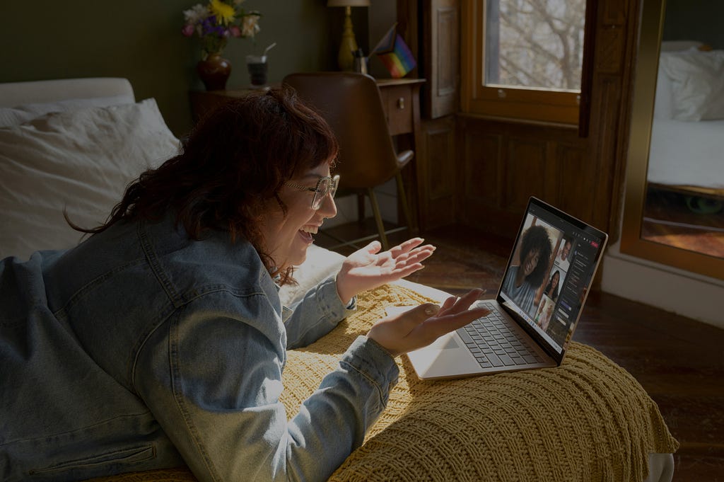 A happy person connecting to others over a video call while lying in her bed.