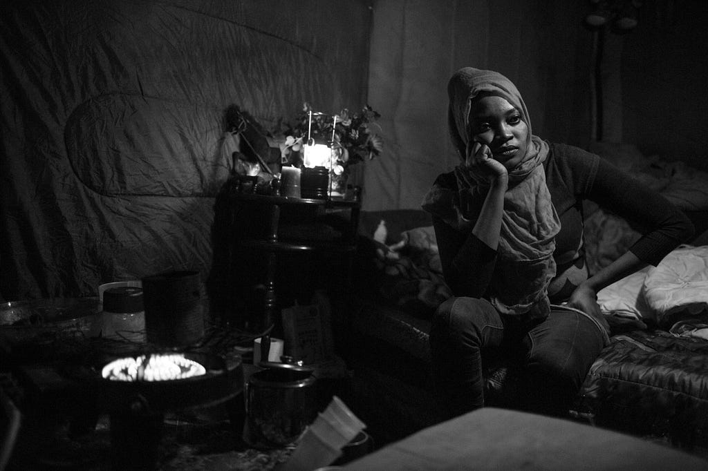Luna in a reflective mood between cooking meals on a portable propane gas ring and caring for her daughter Euro in a shack insulated by donated sleeping bags, which was built by her husband Hosni. She is one of the many women in the Jungle seeking refuge.