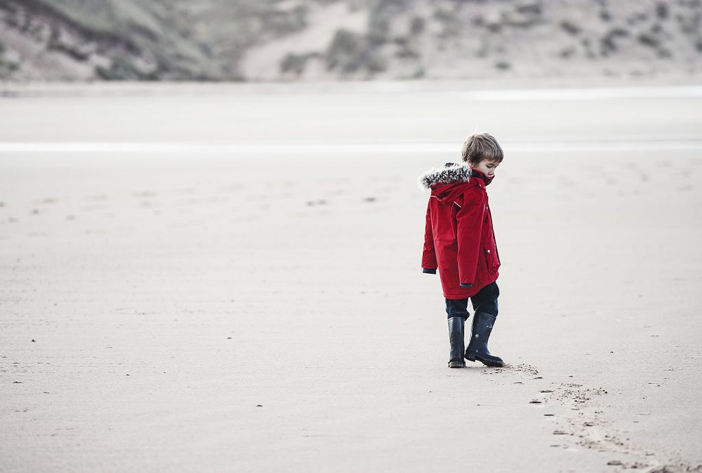 A child is wandering on white sand, leaving footprints.