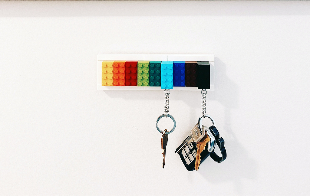 A couple of keys are suspended  from a row of colorful legos that form a key hook.