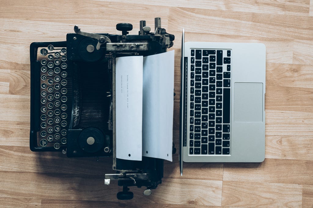 A typewriter with paper next to a modern laptop.