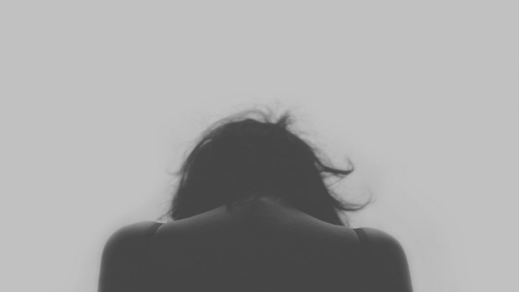 Black and white close up of back of woman with head down, shot from shoulders up