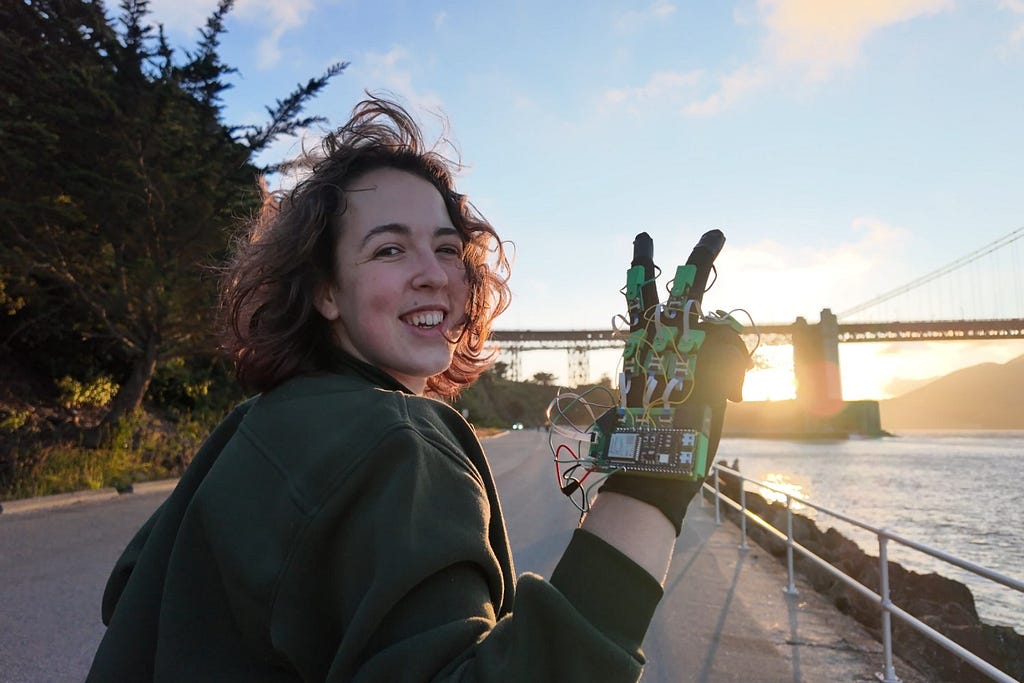 Photo of a smiling young woman posing with her VR glove outside at sunset.