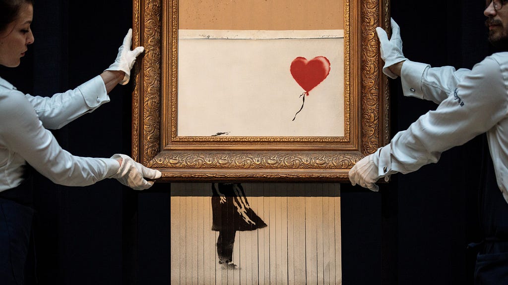 Photo of Banksy’s painting “Girl with Balloon” after it’s been shredded. It’s carried by 2 Sotheby’s employees, taking care of the newly created piece of art called “Love Is in the Bin”, carrying the art-piece with white gloves and showcasing it.