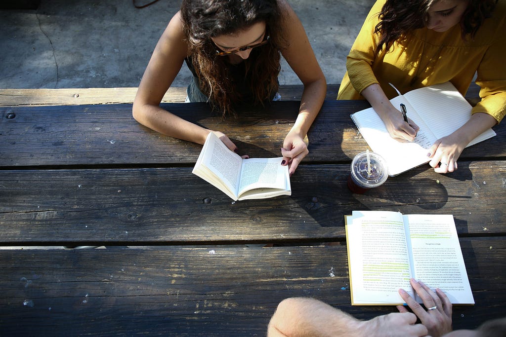 Three people at a table reading and writing.