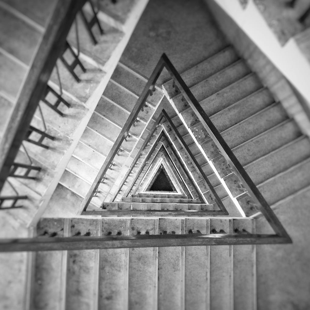 Black and white photo looking down a triangular spiral staircase.