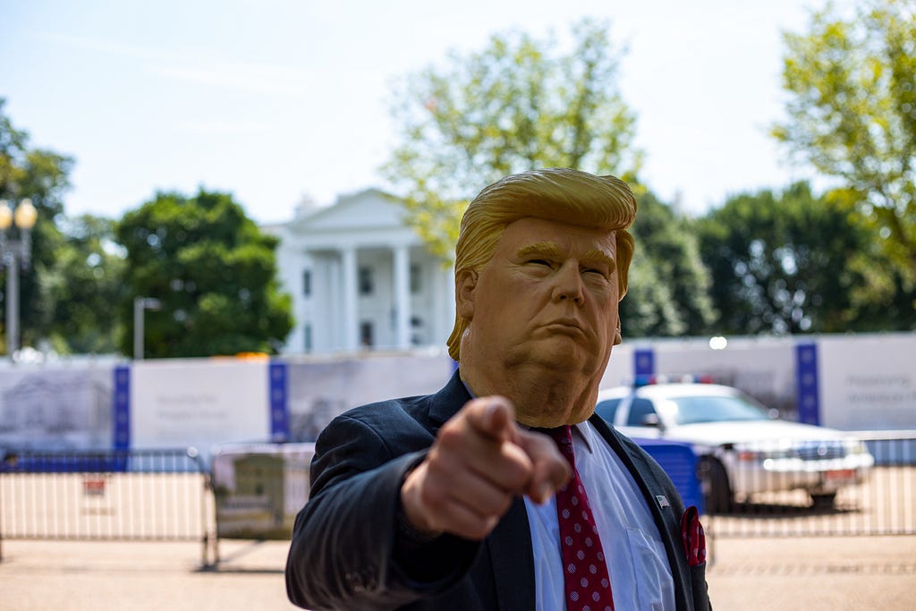 A person wearing a Donald Trump mask and pointing at the camera.