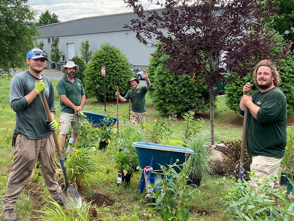 A team of volunteers, standing with their garden tools, smile for a photo while working on the pollinator garden at the observatory.