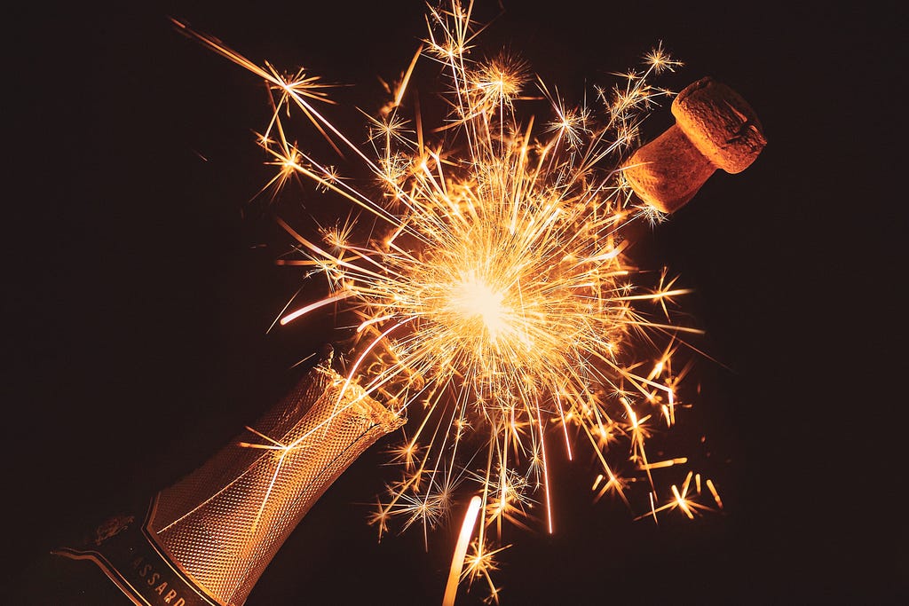 A hand holding a bottle of champagne with fireworks coming out of the bottle.