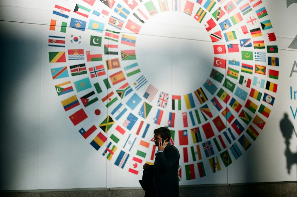 Man on a phone walking by a mural of the world’s flags