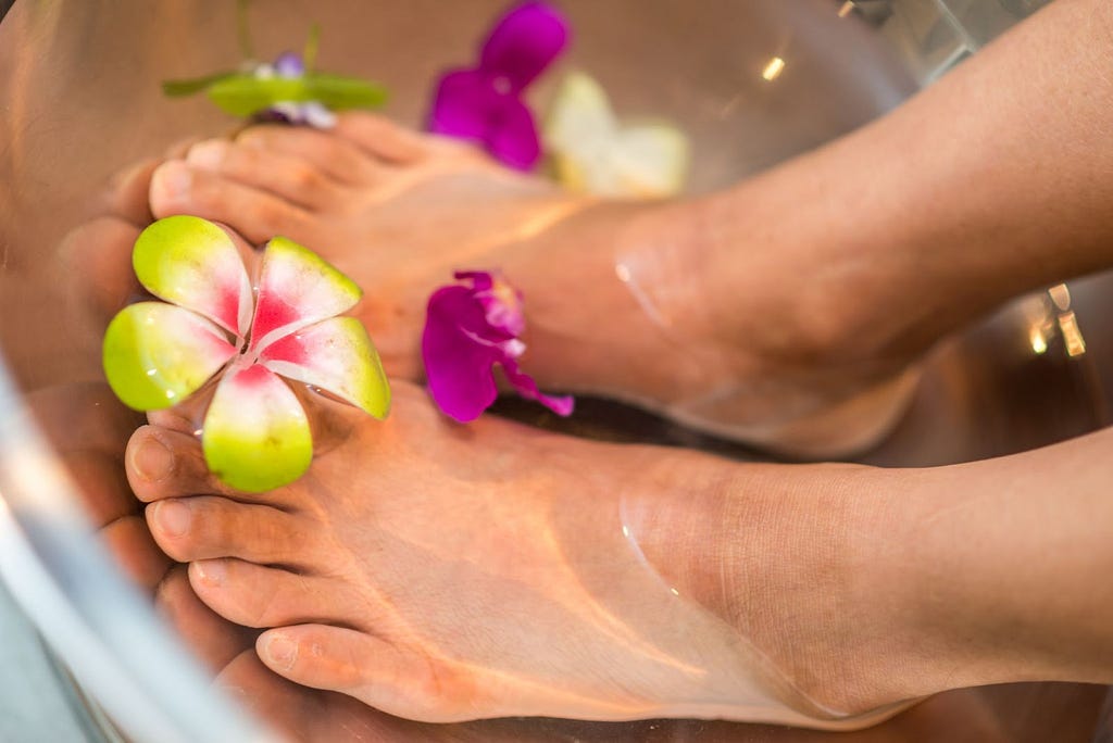 Feet soaked in water containing flowers.