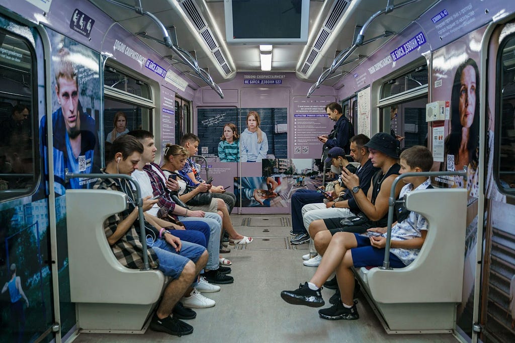 Several people sit on benches on either side of a subway car where the walls are covered with messages from a campaign about human trafficking.